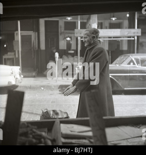 Ein älterer Mann wärmt seine Hände über einem Feuer in den 1950er Jahren durch ein Fenster in Philadelphia zu sehen. Stockfoto