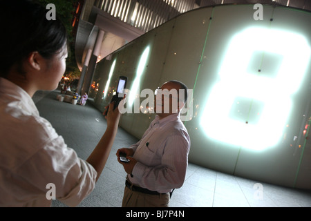 Japaner mit Mobiltelefon vor Digital Nummer Anzeige, Roppongi, Tokyo, Japan. Stockfoto