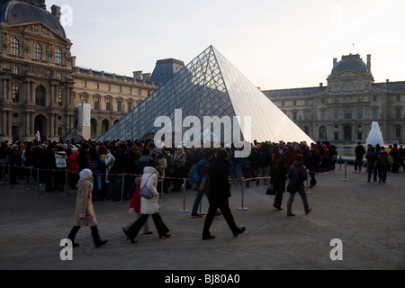 Menschen in die Warteschlange im Morgengrauen zum kostenlosen Eintritt in das Louvre Museum / Musée / Palais du Louvre, neben der Glaspyramide. Paris, Frankreich. Stockfoto