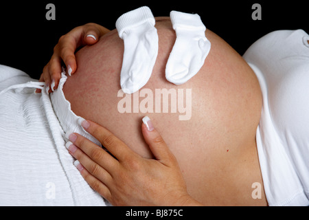 8 Monate schwangere Frau 30 Jahre alt mit Babybauch und kleine Babysocken Stockfoto