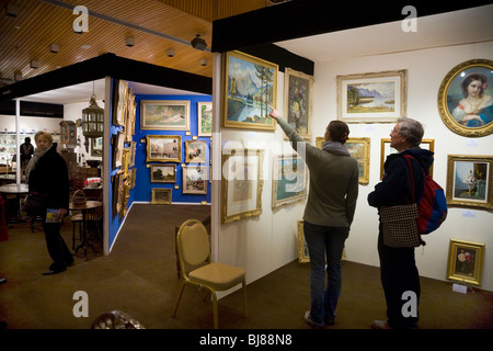 Aussteller / Stall zu verkaufen, antike Gemälde & zwei Kunden auf der & Kunst Antiquitäten Messe, Kensington Town Hall. London. UK Stockfoto