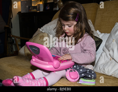 dh Girl Computer Kleinkind Kinder Großbritannien kleines Mädchen 2 Jahre altes Spielzeugkind allein zu Hause mit einem rosafarbenen Laptop Spielzeug Stockfoto