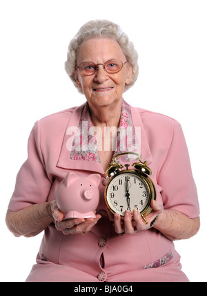 Ältere Frau hält Sparschwein und Uhr über weißen isoliert Stockfoto