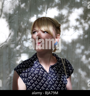 Porträt der jungen blonden Frau im Schatten eines Baumes gegen eine weiße Wand schauen besorgt Stockfoto
