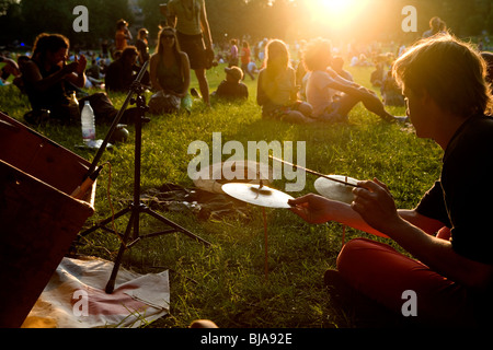 junger Mann spielen Mini-Drum-Kit auf dem Rasen in einem Park bei Sonnenuntergang Stockfoto