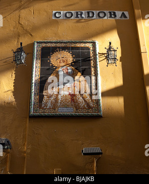 Streetsign buchstabieren Cordoba und gekachelte Bild des religiösen Symbols auf gelbe Wand in Spanien Stockfoto
