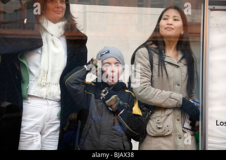 Kind zieht Gesicht und seine Zunge bei einem Fotografen an einer Bushaltestelle in London, Vereinigtes Königreich. Stockfoto