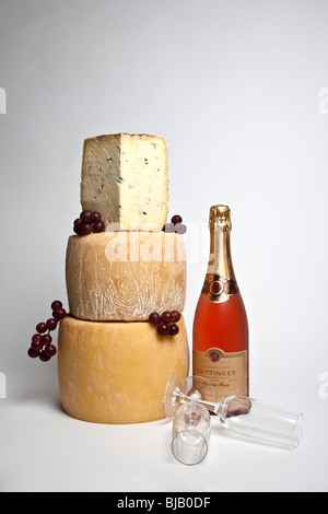 Ein Feier-Turm der ganzen Runde Käse mit einem großen Keil von Blauschimmelkäse mit einer Flasche Champagner und zwei Gläser Stockfoto