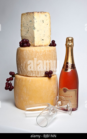 Ein Feier-Turm der ganzen Runde Käse mit einem großen Keil von Blauschimmelkäse mit einer Flasche Champagner und zwei Gläser Stockfoto