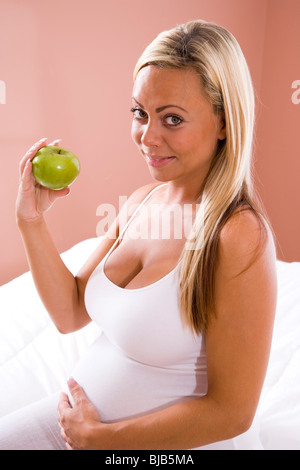 Junge, blonde schwangere Frau entspannen Zuhause Essen Apfel Stockfoto