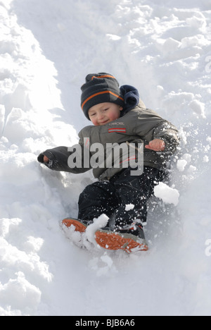 Lachendes Kind junge rutscht ein Schnee bedeckt Hill und spielen im Schnee Stockfoto