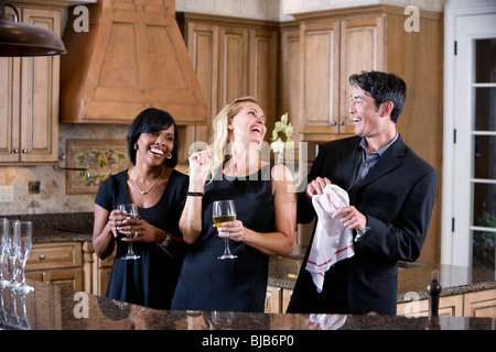 Drei multi-ethnischen Erwachsene Freunde lachen zusammen in Küche, Wein zu trinken Stockfoto