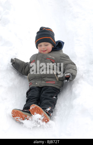 Lachendes Kind junge rutscht ein Schnee bedeckt Hill und spielen im Schnee Stockfoto