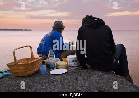 Zwei junge Männer Essen ein Picinic auf einer Klippe direkt am Meer in den Schären von Stockholm. Stockfoto