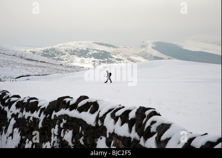 Einsame Figur Wandern im Schnee bedeckt Landschaft, Derbyshire, Peak District, Großbritannien Stockfoto