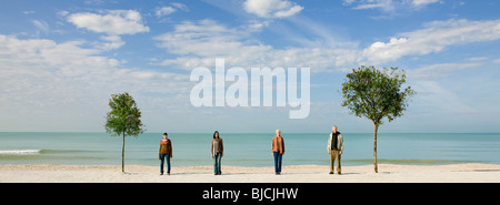 Gruppe von Menschen stehen in Reihe zwischen zwei Bäume am Strand Stockfoto