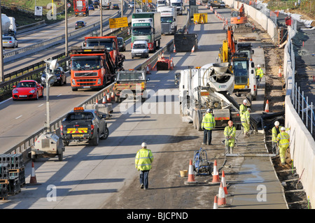 Aus der Vogelperspektive M25 Motorway London Orbital Route hochsichtbare Arbeiter, die Beton verlegen und auf vier Fahrspuren im Gegenverkehr in Essex England Großbritannien erweitern Stockfoto