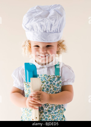 Kleines Mädchen trägt eine Kochmütze und Löffel hält. Stockfoto