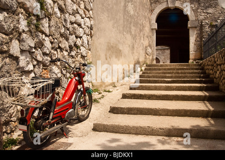 Alte rote Moped durch die Steinmauer den konvergierenden Weg führt zum Bestandteil der ummauerten Stadt gewölbte Eingang geparkt. Stockfoto