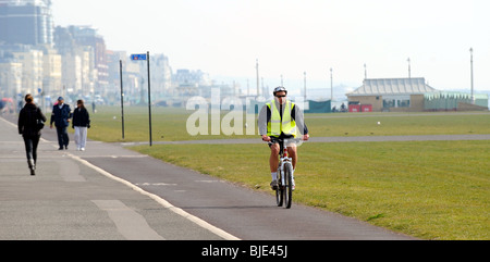 Mann Radfahren entlang Hove Strandpromenade mit einer hohen visability zeigen gelbe Jacke UK Stockfoto