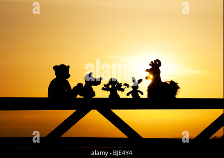 Rag Doll, Huhn, Fuchs, Hase und Stofftiere sitzen auf ein Tor bei Sonnenuntergang in der englischen Landschaft zu tragen. Silhouette Stockfoto
