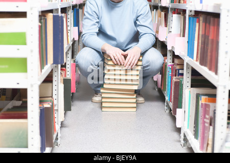 Junger Mann hockt mit Stapel Bücher in der Bibliothek Stockfoto