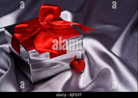 Valentine Geschenk mit Zierband rot auf Silber Seide Hintergrund Stockfoto