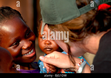 Ein Tourist wird von einer Dame mit ihrem Baby in Mfuwe Village begrüßt. Mfuwe, Sambia. © Demelza Cloke Stockfoto