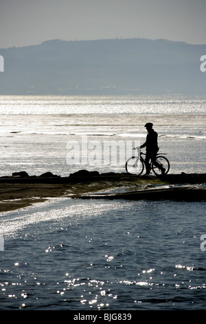 Stadt von West Kirby, England. Silhouette Blick auf eine einsame Radfahrer zu Fuß in der Nähe der Marine See West Kirby. Stockfoto