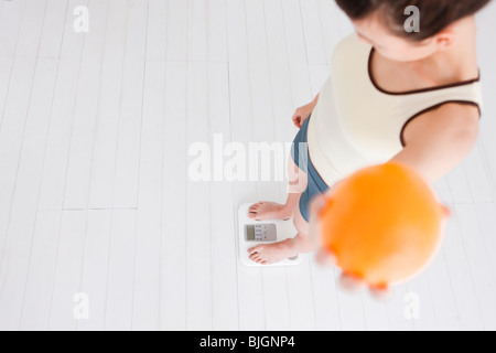 Frau hält eine Orange und wiegen sich auf Waage Stockfoto