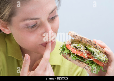 Junge Frau Holding Sandwich und leckte ihr finger- Stockfoto