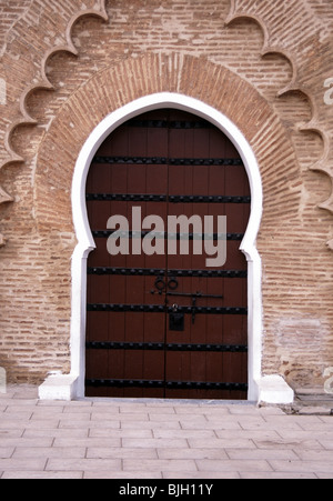 Marokko. Schwere hölzerne Tür mit eisernen Nieten oder Nieten, die den Eingang zu einem Gebäude bieten, das von kunstvollen dekorativen Ziegelmauern umgeben ist. Der Hufeisenbogen oder der maurische Bogen der marokkanischen Türen sind eine der häufigsten Formen in der Architektur des Landes. Als ikonisches Merkmal der islamischen Architektur ist das Design smiliar zu einem Schlüsselloch, daher wird es nur als Schlüssellochbogen bezeichnet. Stockfoto