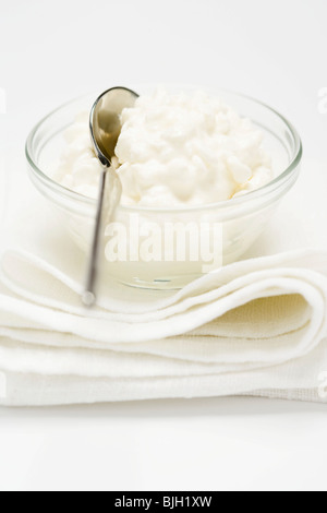 Hüttenkäse in kleine Glasschale mit Löffel auf Tuch- Stockfoto