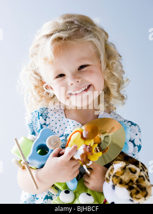 kleines Mädchen hält einen Arm voll ihr Spielzeug Stockfoto