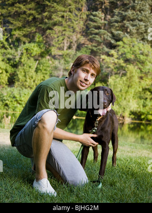 junger Mann kniend mit einem chocolate Labrador retriever Stockfoto