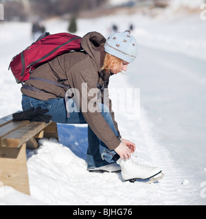 Frau schnürung oben ihre Schlittschuhe im Freien, Assiniboine River Trail, Winnipeg, Manitoba, Kanada. Stockfoto