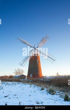 Die schiefen Hardley Entwässerung Mühle an der ersten Ampel nach Winter Schneefall auf den Norfolk Broads Stockfoto