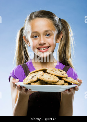 Mädchen schaut in die Kamera halten einen Teller mit chocolate Chip cookies Stockfoto