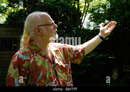 weißen Haaren Gentleman mit Bart & Pony Tail tragen Hawaiihemd erstreckt sich Arm oder Wellen in der Geste der Freundschaft im Garten Stockfoto