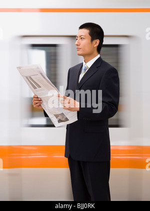 Geschäftsmann, lesen Zeitung mit u-Bahn im Hintergrund Stockfoto