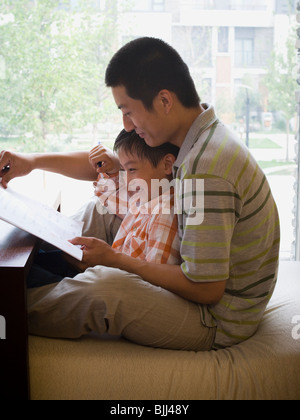 Mann und der Junge sitzt und liest vor große Fenster Stockfoto