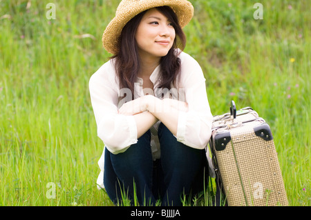 Frau sitzt im Feld mit Koffer Stockfoto
