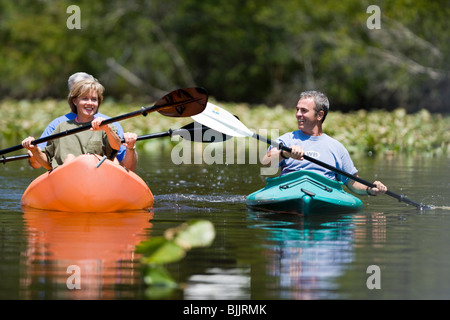 Freunde paddeln Kajaks in der Nähe von Lilly Pads in einem Binnenschiff Stockfoto