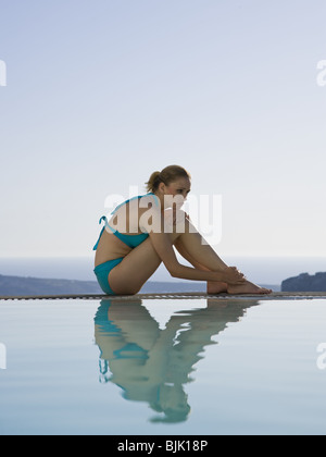 Frau im Badeanzug sitzt am Rand des Infinity-Pool im freien Stockfoto