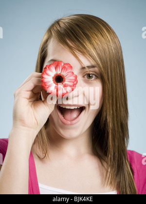 Nahaufnahme der Holding Blume bis zu ihrem Auge lächelnde Frau Stockfoto