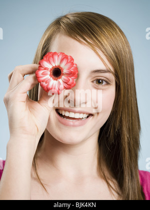 Nahaufnahme der Holding Blume bis zu ihrem Auge lächelnde Frau Stockfoto
