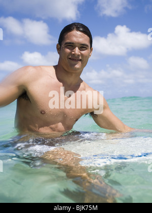 Mann sitzt auf Surfbrett im Wasser lächelnd Stockfoto