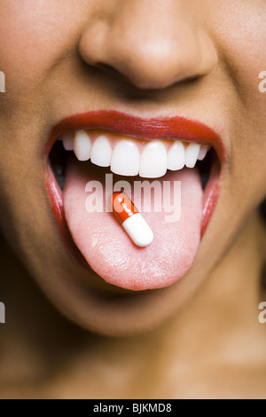 Frau mit rotem Lippenstift mit einer Pille auf Zunge Stockfoto