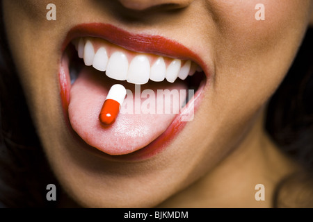 Frau mit rotem Lippenstift mit einer Pille auf Zunge Stockfoto