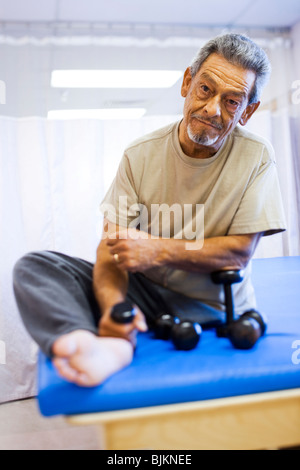 Mann mit einem Bein sitzen und Training mit Gewichten Stockfoto